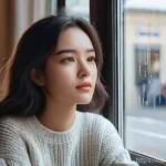 Home 5 웹툰작가가 꼭 읽어야 할 책 - **A thoughtful young woman**, mid-20s, with long, wavy dark hair, sitting at a window seat in a cozy...